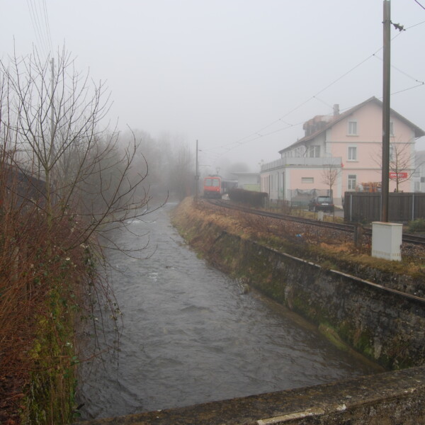 Augstbach-Fluss neben Bahngleisen an einem nebligen Tag.
