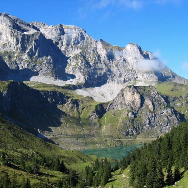 Bannalpsee: Berglandschaft mit grünem See und schroffen Felsen unter blauem Himmel.