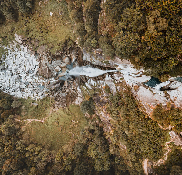 Luftaufnahme des Flusses Bavona, der durch Felsen und Wald fließt.