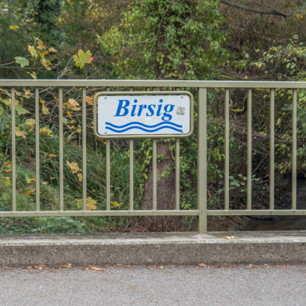 Birsig-Schild auf einer Brücke über den Fluss. Der Name des Flusses ist auf dem Schild abgebildet.