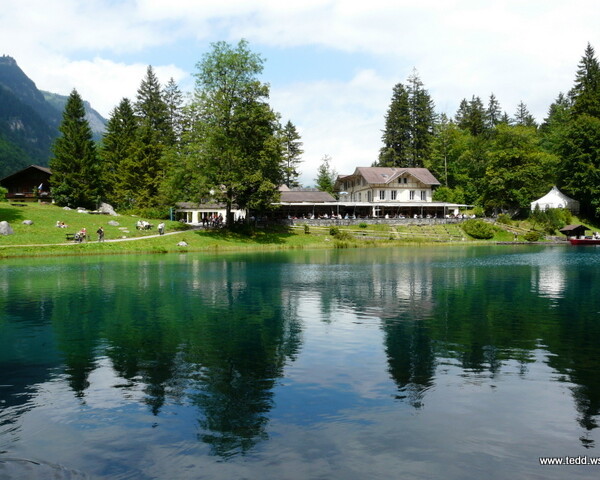 Blausee Kandergrund: Türkisblauer See mit Spiegelung von Bäumen und einem Hotel.