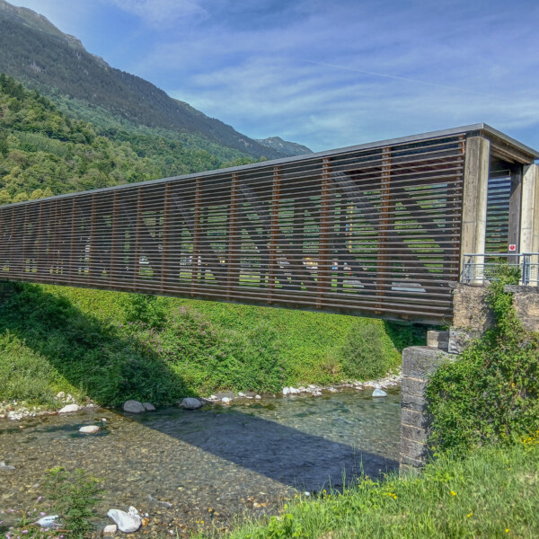 Moderne Brücke über Fluss in Brenno, umgeben von grüner Natur und Bergen.