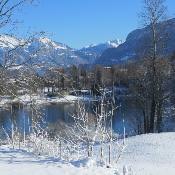 Verschneiter Burgseeli (Ringgenberg) See mit Bergen im Hintergrund unter blauem Himmel.
