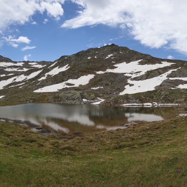 Lai da Chazfora: Bergsee mit Schneeflecken und Spiegelung unter blauem Himmel.