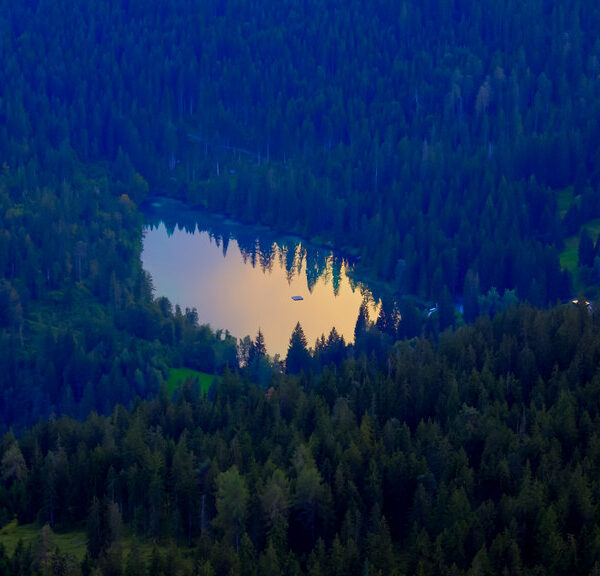 Crestasee, ein Bergsee umgeben von dichten grünen Wäldern, spiegelt den Himmel wider.