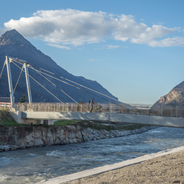 Fußgängerbrücke über die Drance mit Bergkulisse.