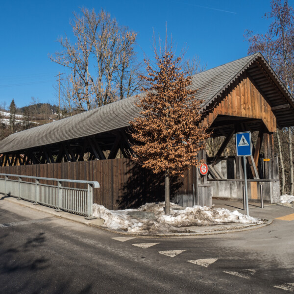 Gedeckte Holzbrücke in Entlen, Schweiz, mit Fußgängerweg-Schild und Schnee.