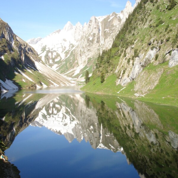 Fälensee: Spiegelglatter Bergsee umgeben von schneebedeckten Gipfeln und grünen Hängen.