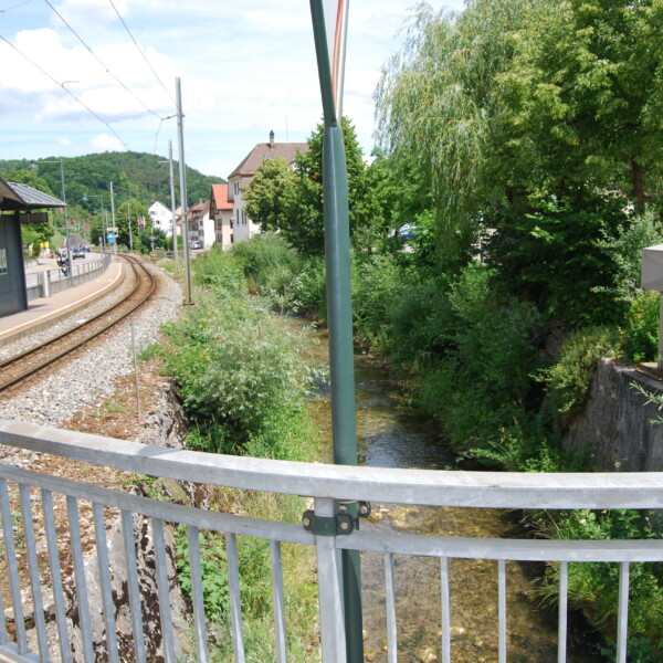 Haltestelle Frenke an Bahngleisen mit Bach und grüner Landschaft.