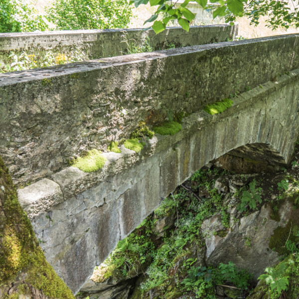 Alte Steinbrücke mit Moos bewachsen, eingebettet in üppiges Grün. Gadmerwasser.