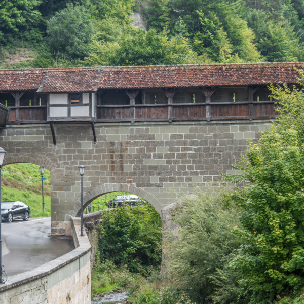 Gedeckte Steinbrücke in Galtera (Gottéron) mit Straße und Bewaldung.