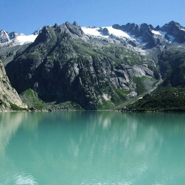 Türkisblauer Gelmersee mit Bergpanorama und schneebedeckten Gipfeln in der Schweiz.
