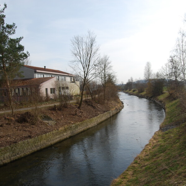 Fluss Glatt in Zürich, flankiert von Uferböschungen und einem Gebäude.