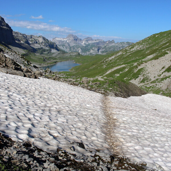 Glattalpsee im Sommer: Schnee bedeckt einen Teil der Berglandschaft mit See und blauem Himmel.