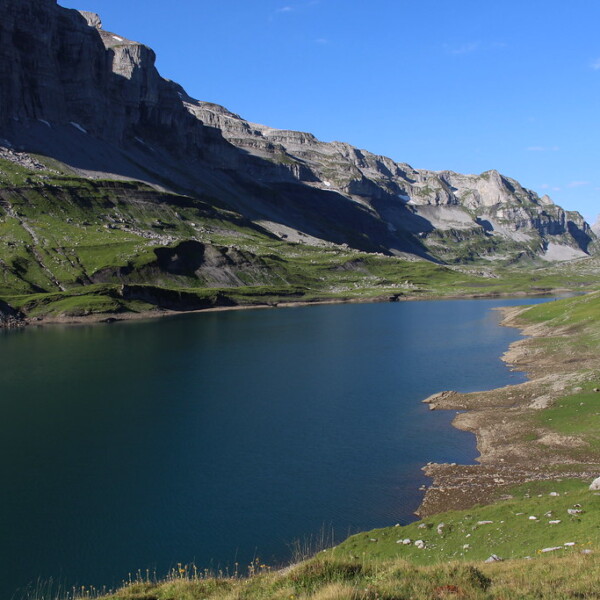 Glattalpsee: Blauer Bergsee umgeben von grünen Wiesen und steilen Felswänden.
