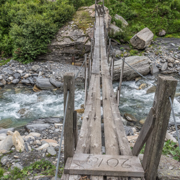 Hölzerne Hängebrücke über einen Fluss im Glenner-Tal. 