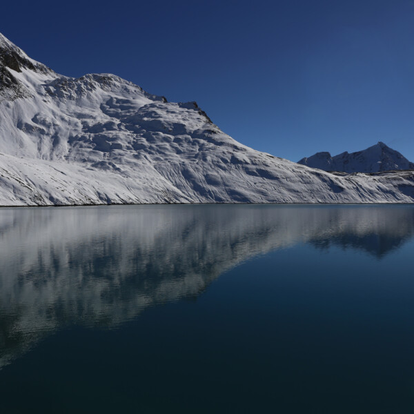 Griessee: Verschneite Berge spiegeln sich im tiefblauen Bergsee.