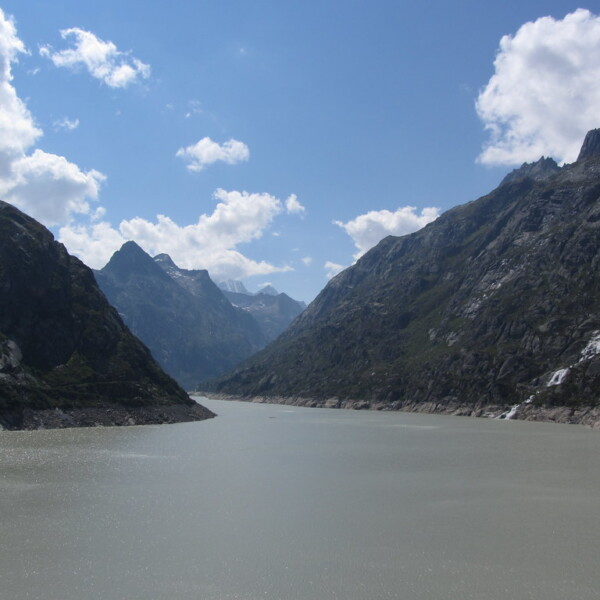 Grimselsee: Bergsee umgeben von steilen Felswänden unter blauem Himmel mit Wolken.