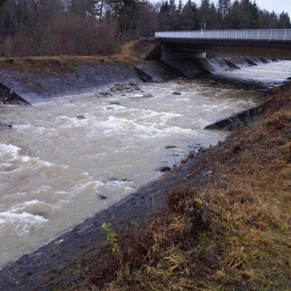 Grosse Schliere Fluss unter Brücke, umgeben von Uferbefestigungen und Vegetation.