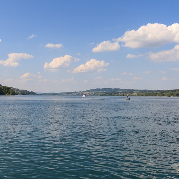Hallwilersee: Ruhige Seeoberfläche mit Booten unter blauem Himmel und Wolken.