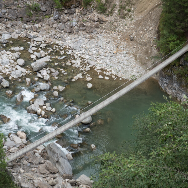 Hängebrücke über den Hinterrhein Fluss, umgeben von Felsen und Vegetation.