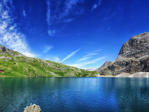 Iffigsee: Bergsee mit grünem Hügel und felsiger Bergkette unter blauem Himmel.