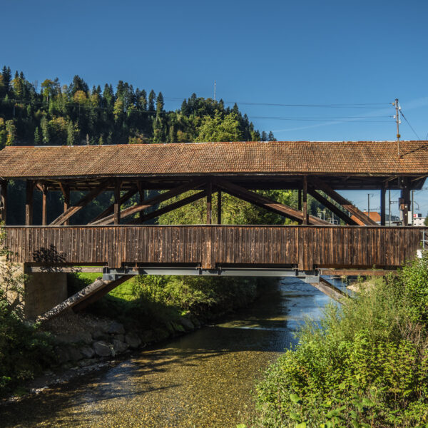 Gedeckte Holzbrücke über den Ilfis-Fluss, umgeben von Bäumen und Grün