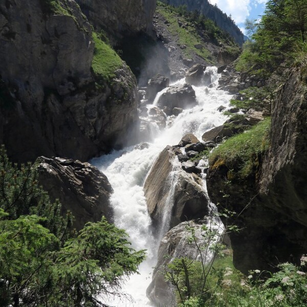 Tosender Wasserfall in Kander, umgeben von Felsen und Grün.