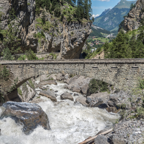 Steinbrücke über den tosenden Fluss in Kander, Schweiz, umgeben von Bergen.