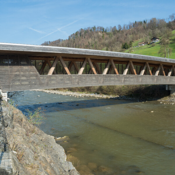 Gedeckte Holzbrücke über die Kleine Emme, Schweiz, mit bewaldetem Hügel im Hintergrund.