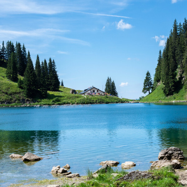 Idyllischer Lac Lioson See mit Hütte am Ufer und grünen Hügeln unter blauem Himmel