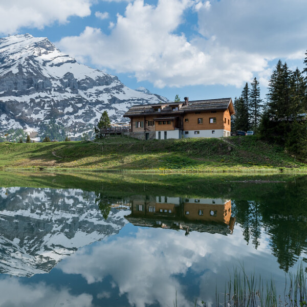 Lac Retaud Spiegelung mit Chalet und schneebedeckten Bergen im Hintergrund.