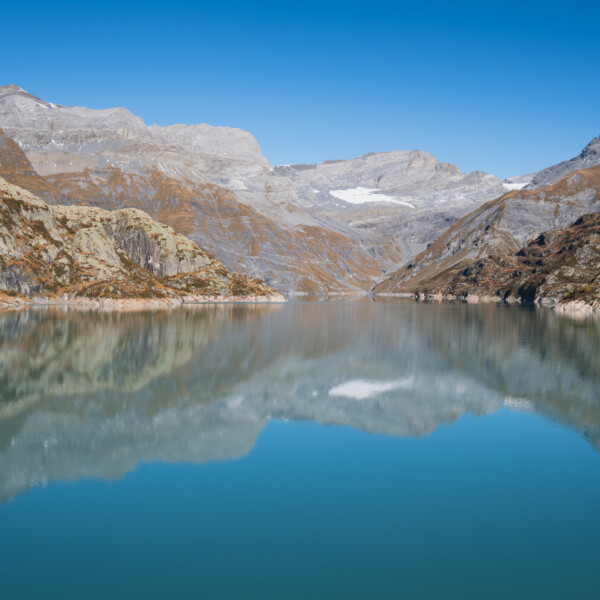 Lac d'Emosson: Bergsee mit Spiegelung der umliegenden Berge unter blauem Himmel.