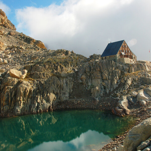 Lac d'Orny mit Berghütte am Ufer, umgeben von Felsen und blauem Himmel.
