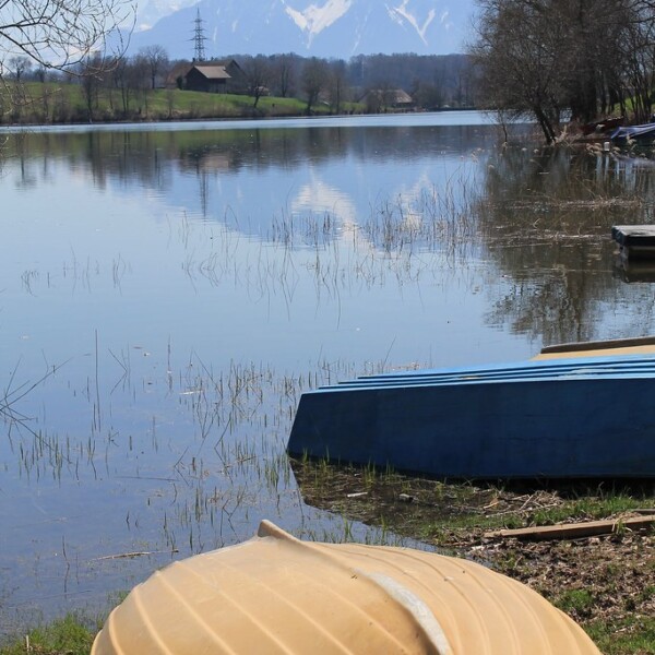 Gelbe und blaue Boote am Ufer des Lac de Bret mit Bergpanorama im Hintergrund.