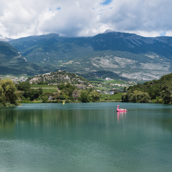Lac de Géronde: Ruhiger See mit Bergen im Hintergrund und einem rosa Flamingo-Boot.