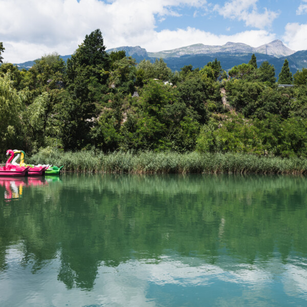 Bunte Tretboote auf dem Lac de Géronde, umgeben von grüner Natur und Bergen.