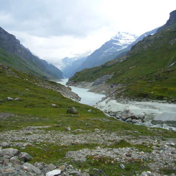 Lac de Mauvoisin: Berglandschaft mit See und Schneebergen unter bewölktem Himmel.