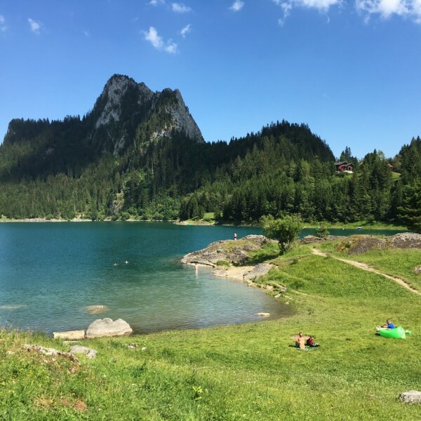 Lac de Tanay: Idyllischer Bergsee mit grüner Uferlandschaft und bewaldeten Bergen im Hintergrund.