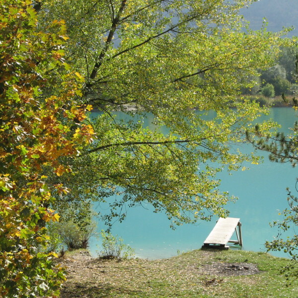Türkisblauer Lac de la Brèche mit kleinem Steg, umrahmt von Bäumen im Herbstlicht.