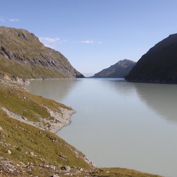 Lac des Dix: Ruhiger Bergsee zwischen grünen Hängen und hohen Bergen unter blauem Himmel.