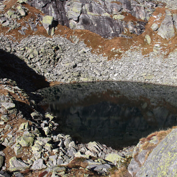 Lago Melo, ein Bergsee umgeben von Felsen und Geröll im Bosco. Reflexionen im Wasser.