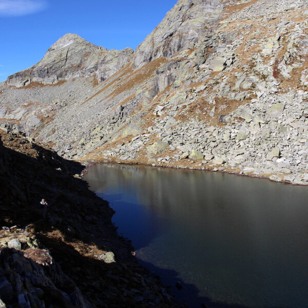 Lago Pero, ein Bergsee umgeben von Felsen und Geröll unter blauem Himmel.