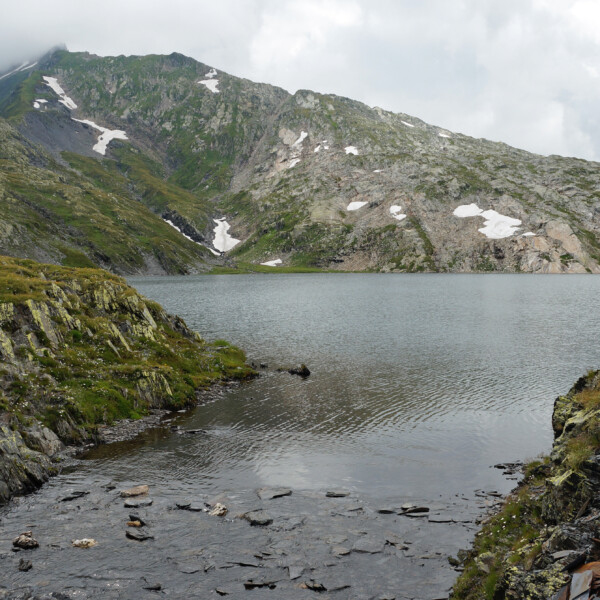 Lago Retico: Bergsee mit schneebedeckten Gipfeln und felsiger Uferlandschaft.
