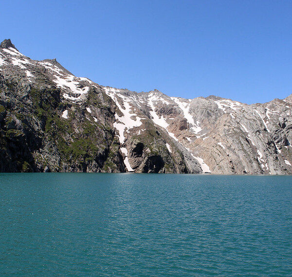Lago dei Cavagnöö mit Bergen und Schnee unter blauem Himmel.