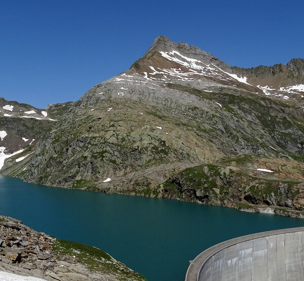 Lago dei Cavagnöö mit Staumauer und Berglandschaft unter blauem Himmel.