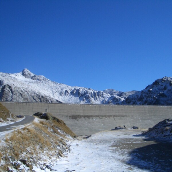 Lago della Sella: Winterlandschaft mit Stausee und schneebedeckten Bergen unter blauem Himmel.