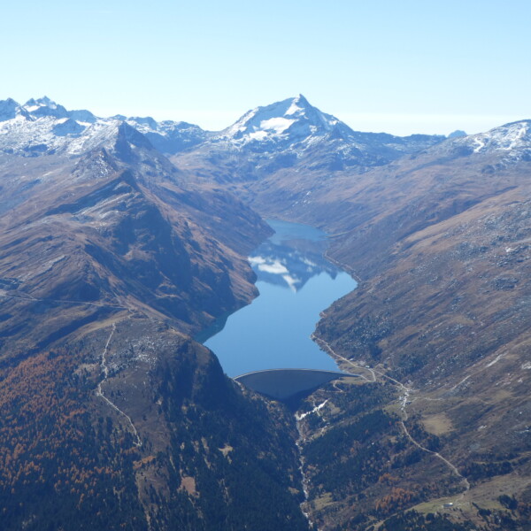 Lago di Lei: Bergsee mit Staumauer und schneebedeckten Gipfeln im Hintergrund.
