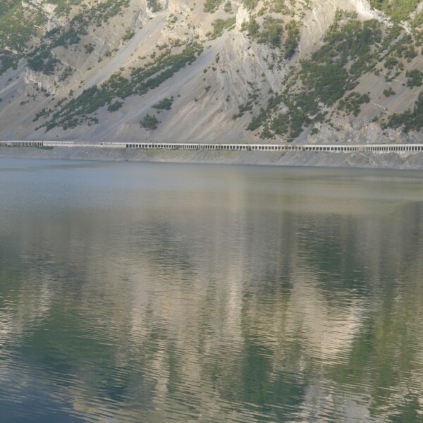 Lago di Livigno: Ruhiger See mit Bergreflektionen und Staumauer.