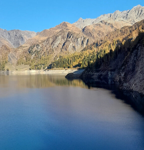 Lago di Luzzone mit Bergen und Herbstwald unter blauem Himmel.